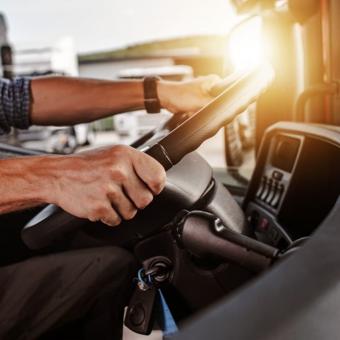 Driver's hands on a truck steering wheel in morning sun