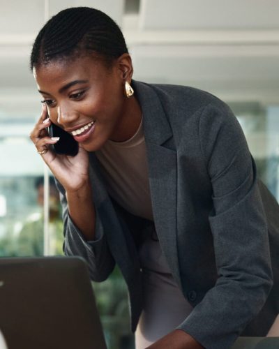 Black woman, phone call and typing on laptop in office, schedule meeting and talking to client. Female person, communication and online for news quote by contact, press journalist and calendar notes.